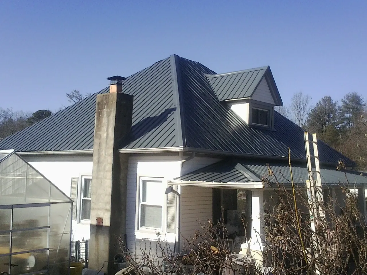 Dark blue standing seam metal roof on a white farmhouse with dormer — Slate & Tile Roof Repair by Roofing Brothers in Mercer Island
