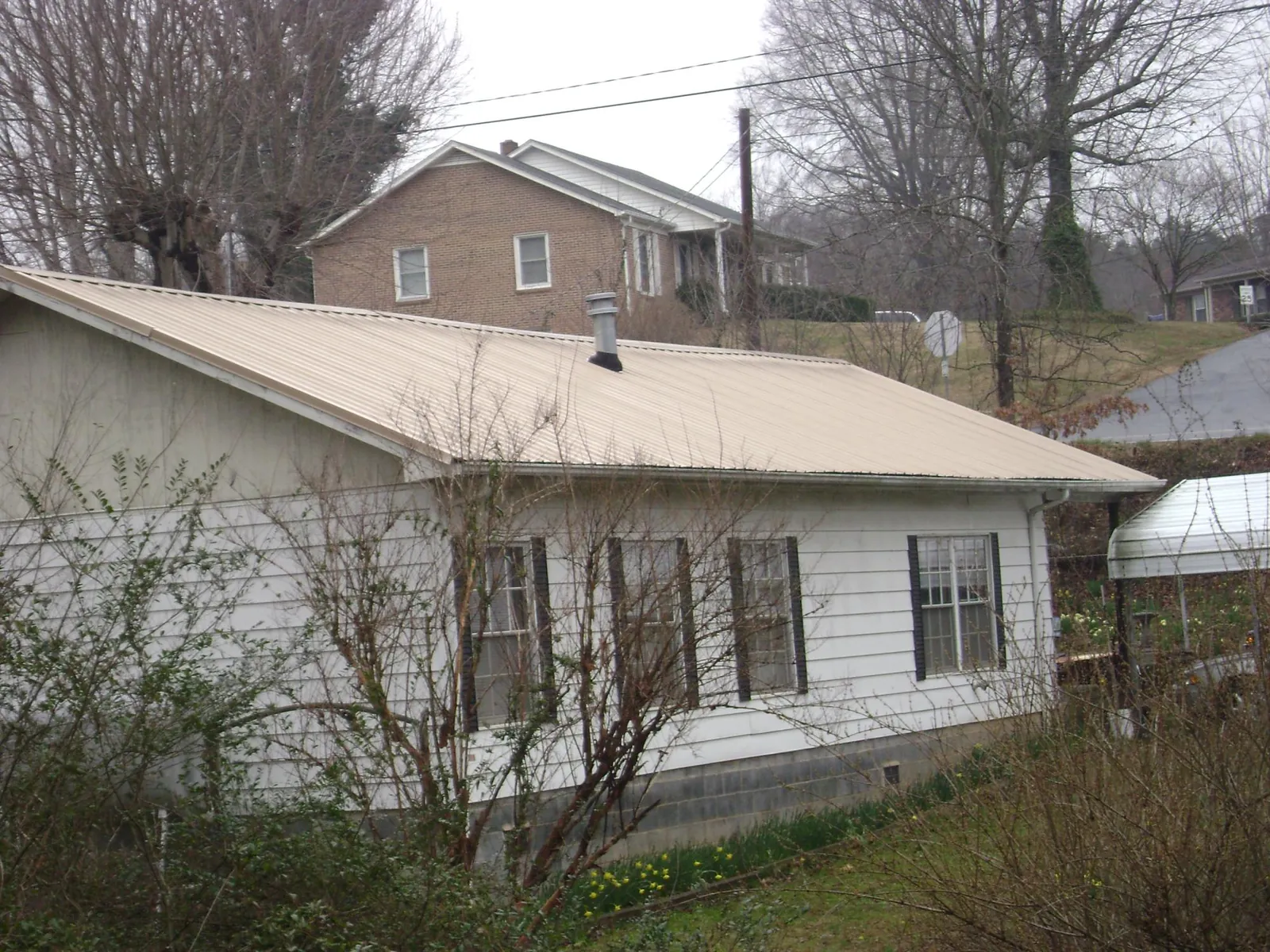Tan metal roof on a white sided house set into a hillside — Commercial Roofing by Roofing Brothers in Mercer Island